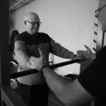 black and white image of male trainer instructing male client on barbell grip