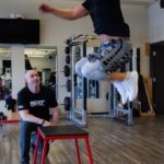 male trainer with male client performing leap onto platform