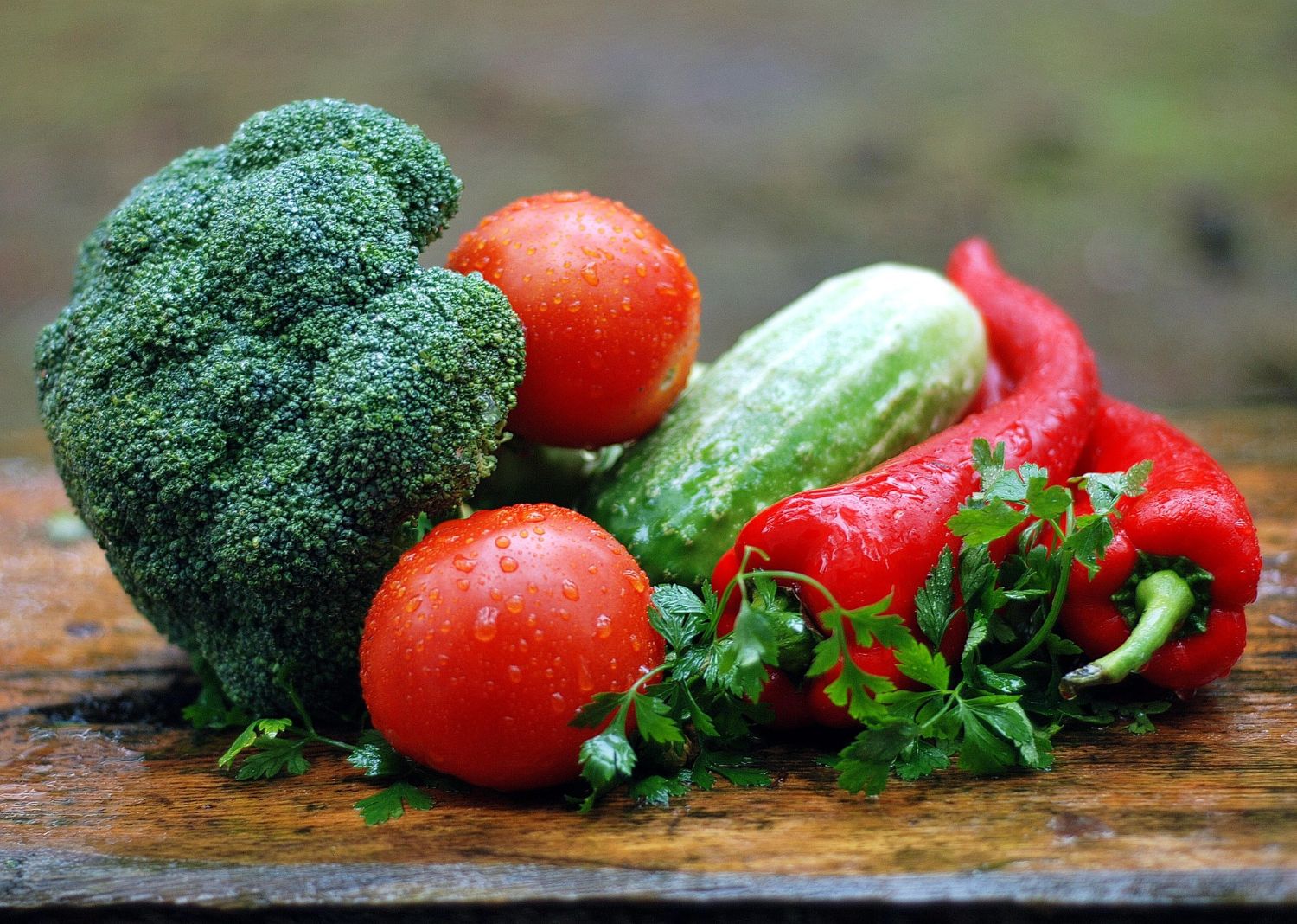 mix of green and red vegetables on an outdoor table, including: broccoli, tomotoes, cucumber, and red peppers